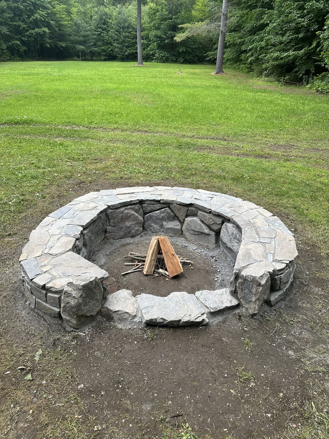 Finished stone fire pit in daylight with firewood laid inside, ready to light